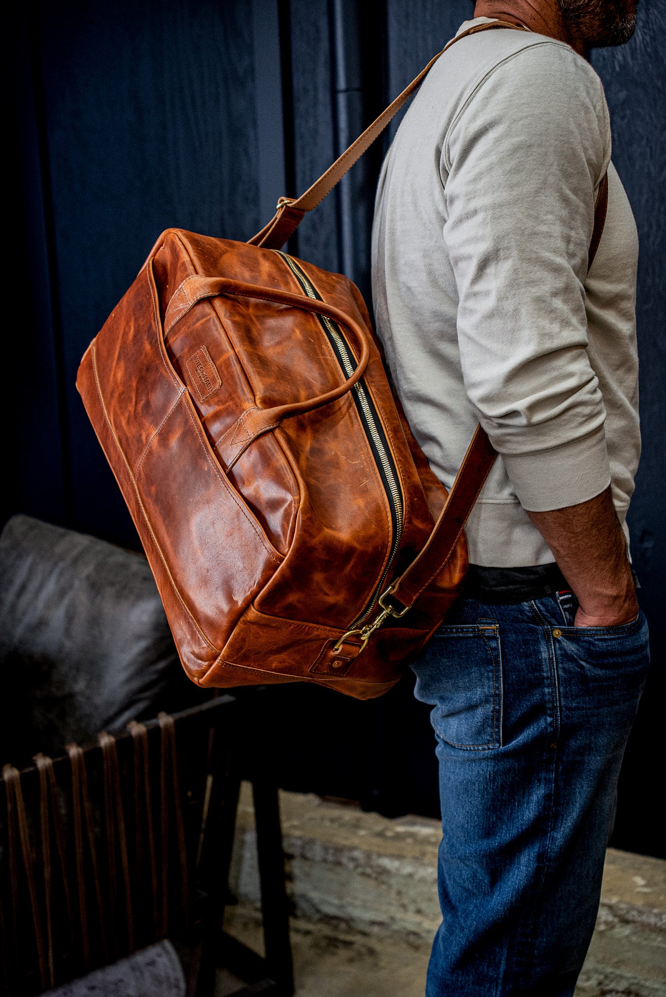 Tan Horween leather weekender bag carried on the shoulder with brass zipper and strap.