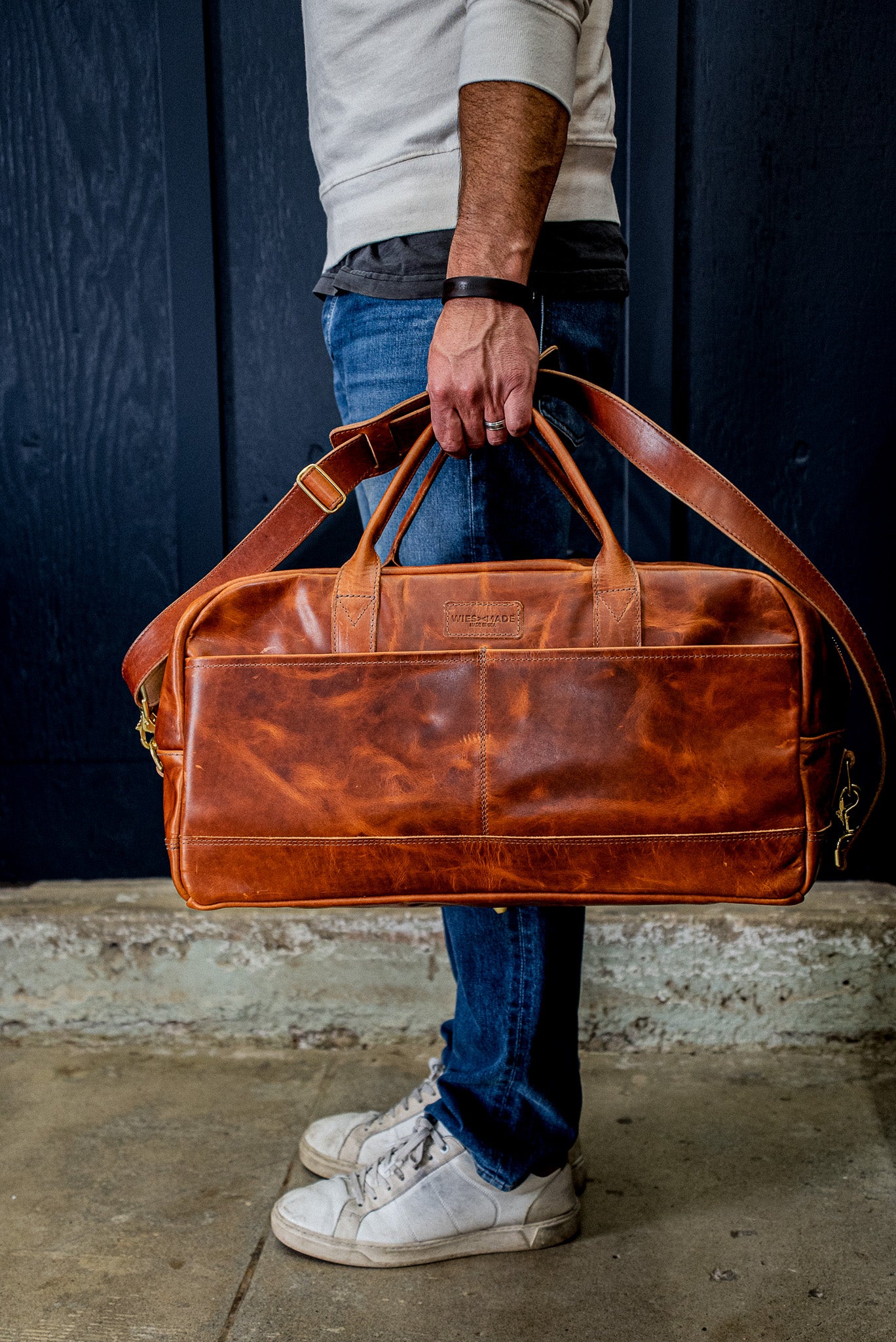 Tan Horween leather weekender bag with brass hardware carried at a person's side.