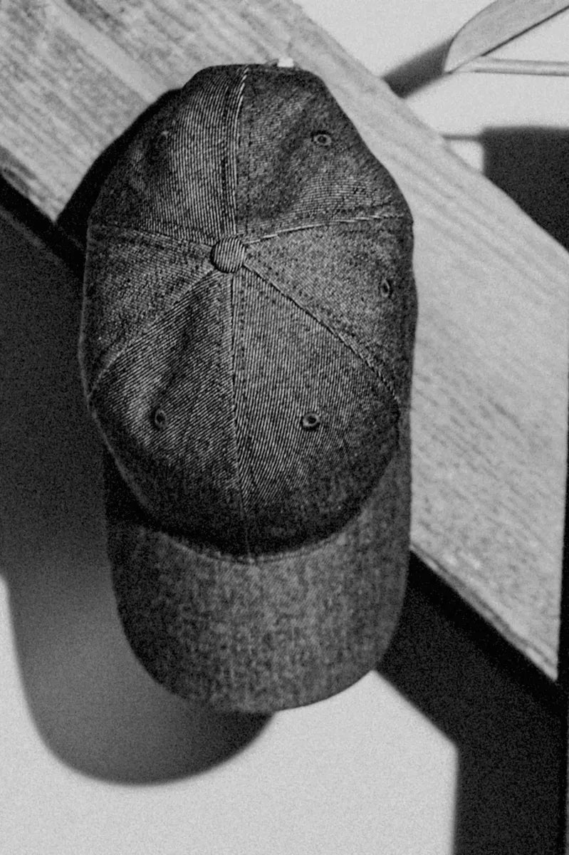 Six-panel selvedge denim ball cap resting against a wooden beam, front view.
