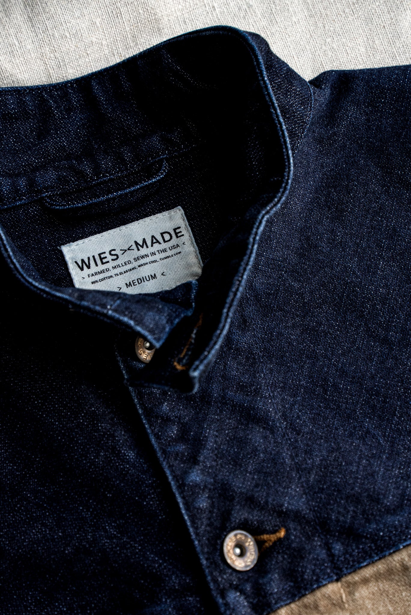 Close-up of indigo broken twill denim vest collar with WiesMade USA-made label and brass button.