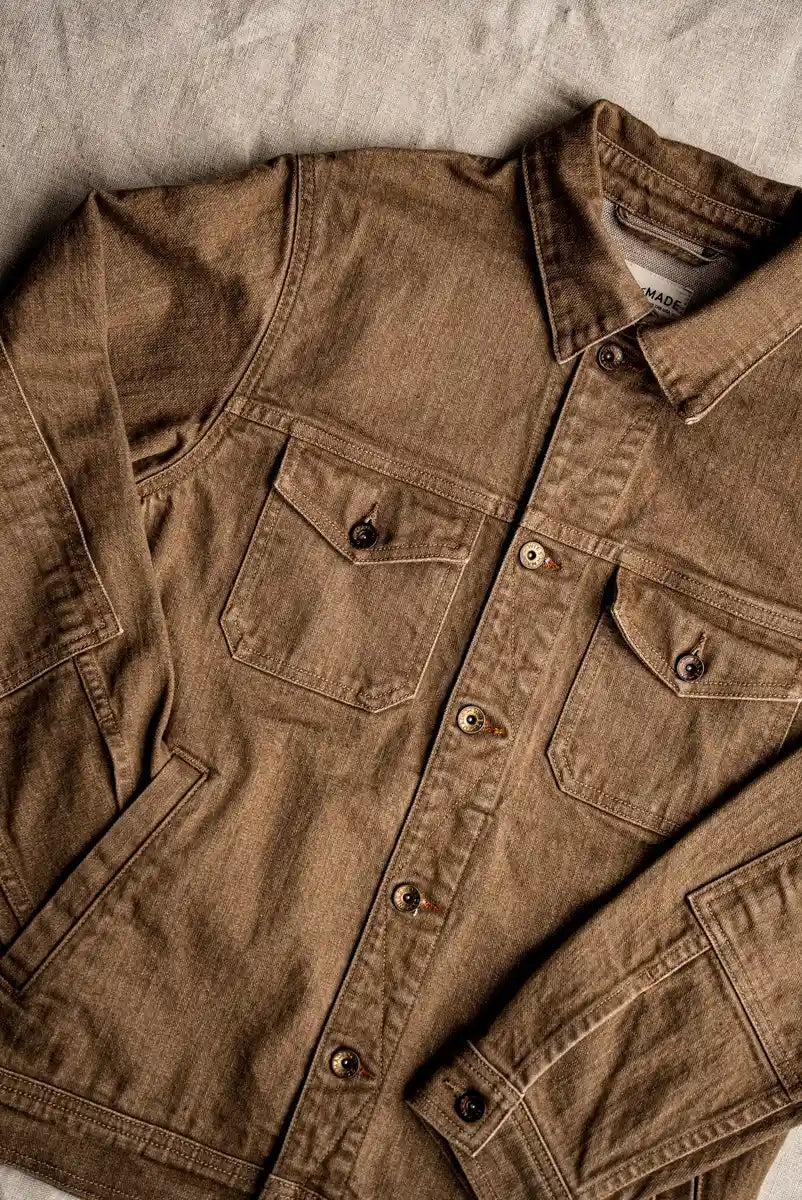 Wheat-colored broken twill denim jacket laid flat, showing chest pockets, brass buttons, and collar detail.