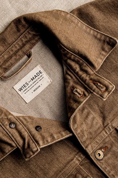 Close-up of wheat-colored broken twill denim jacket showing interior WiesMade label, tobacco buttonholes, and brass hardware.