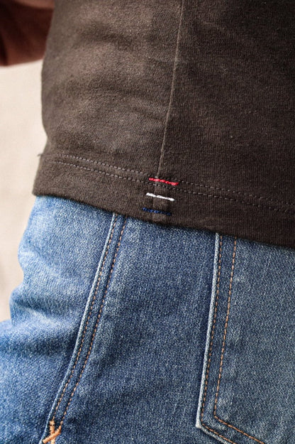 Close-up of basalt brown cotton tank hem with red, white, and blue signature bartacks over blue jeans.