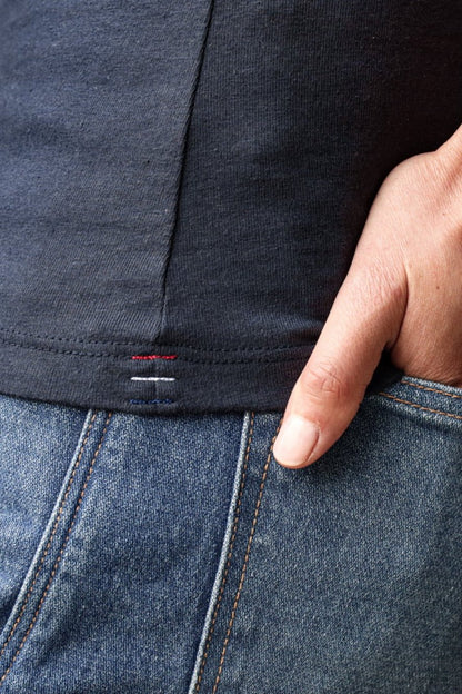 Close-up of the Bolinas cotton tank hem with signature triple bartacks, tucked into denim jeans.