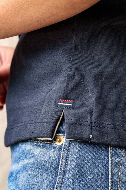 Close-up of the Reyes tank hem showing twill-lined side vent and red, white, and blue signature bartack stitching over denim.