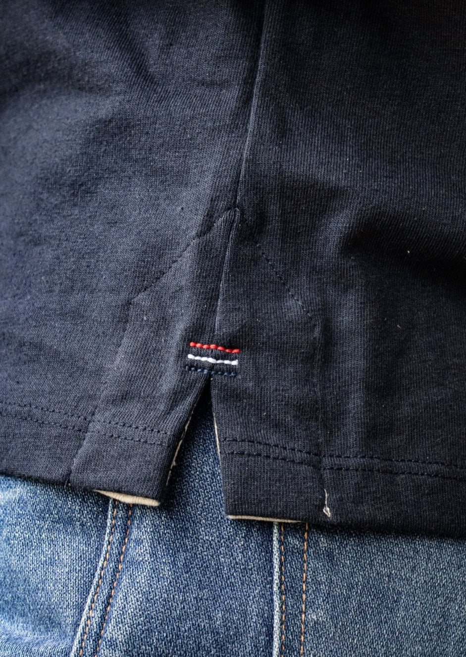 Close-up of the boxy tee's side vent hem with signature red, white, and blue triple bartack stitching, worn over denim jeans.