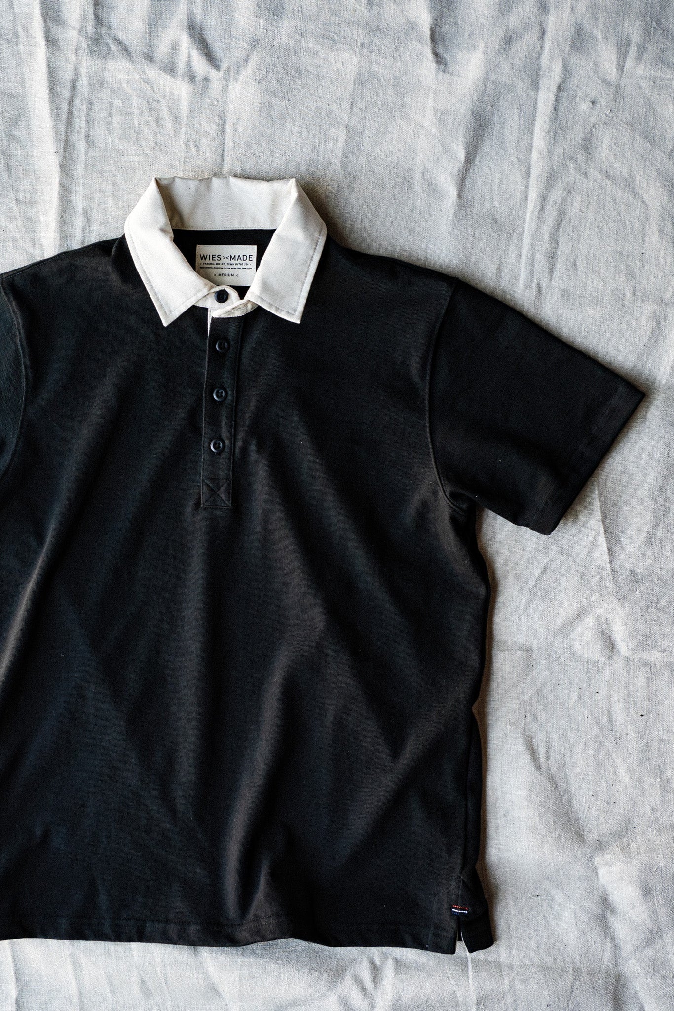 Basalt black short-sleeve rugby jersey with contrasting white collar, laid flat on linen.