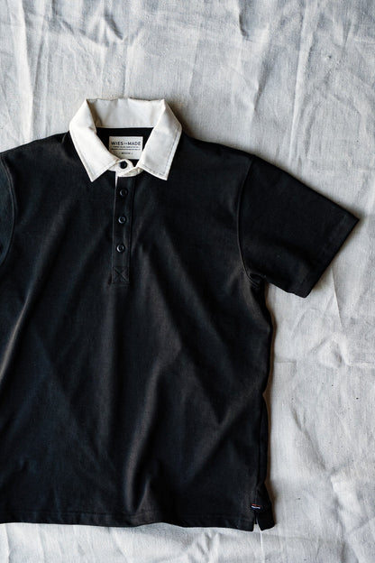 Basalt black short-sleeve rugby jersey with contrasting white collar, laid flat on linen.