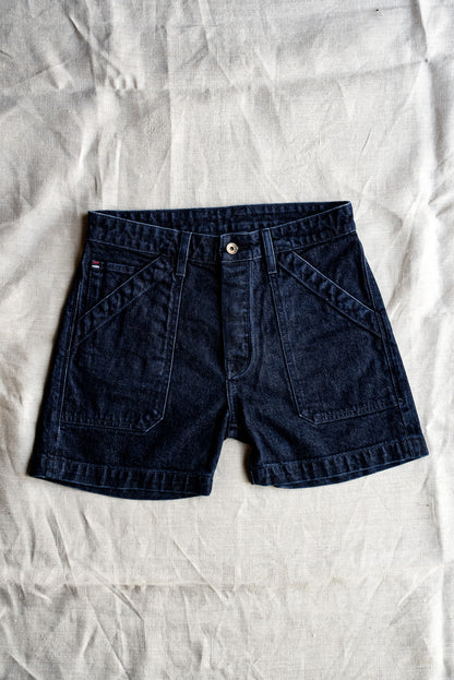 Dark ocean wash denim military shorts with angled front pockets laid flat on linen.