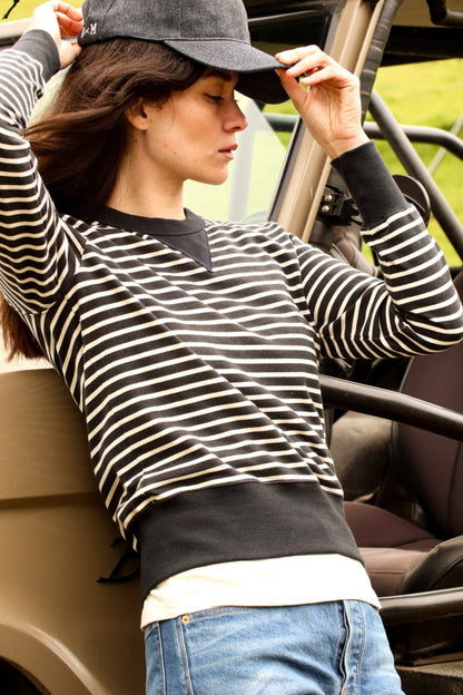 Black and cream striped cotton rugby pullover worn by a woman leaning against a utility vehicle.