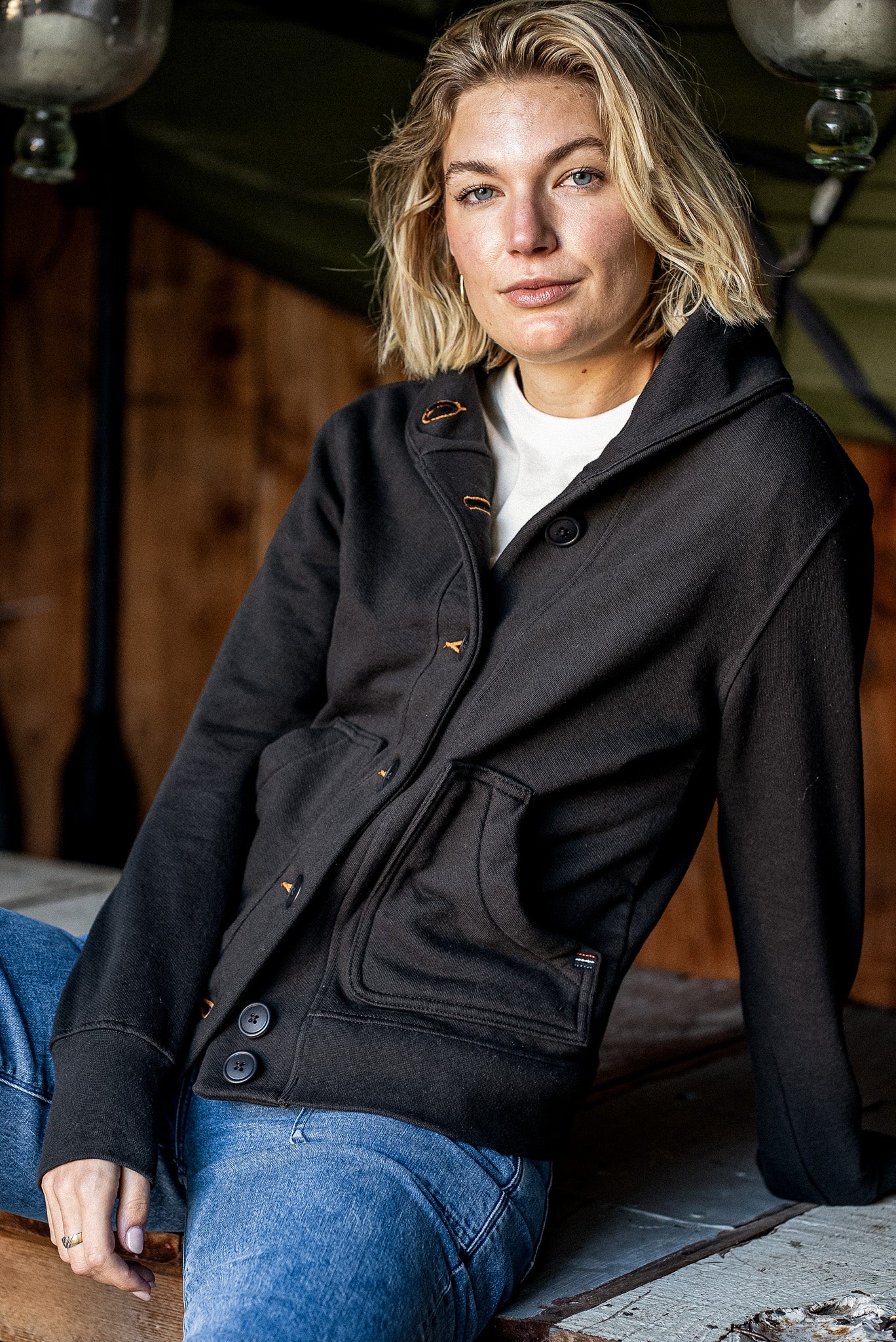 Woman wearing the Bodega shawl collar French terry cardigan in basalt black with tobacco contrast stitching, paired with.