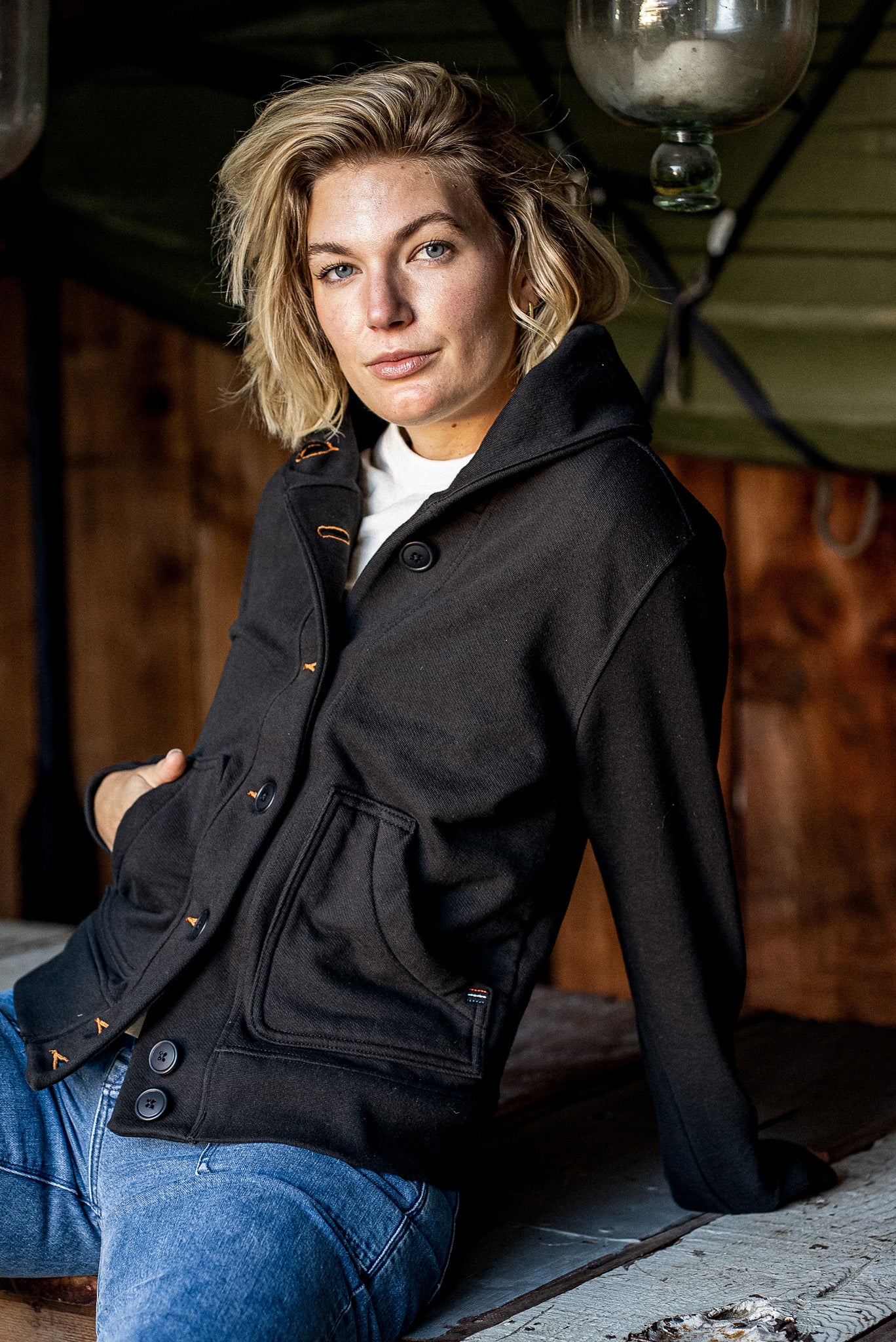 Woman in a black French terry shawl cardigan with orange contrast stitching, paired with blue jeans.