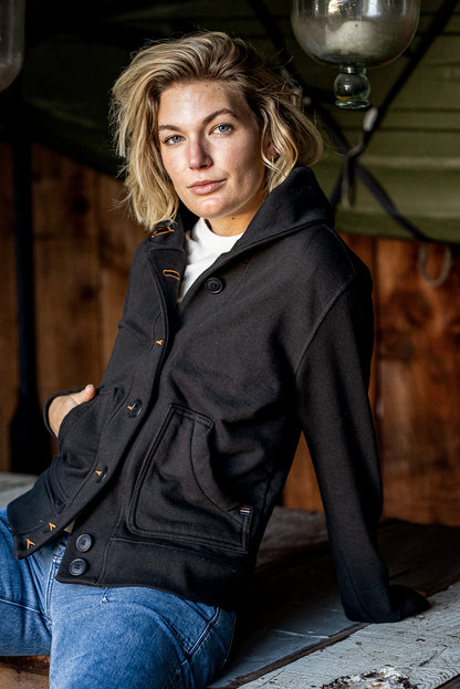 Woman in a black French terry shawl cardigan with orange contrast stitching, paired with blue jeans.