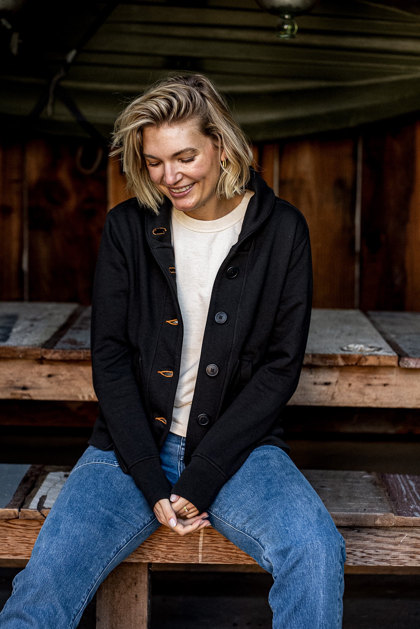 Women's Bodega shawl cardigan in black French terry with tobacco contrast keyholes, worn over a cream tee and jeans.