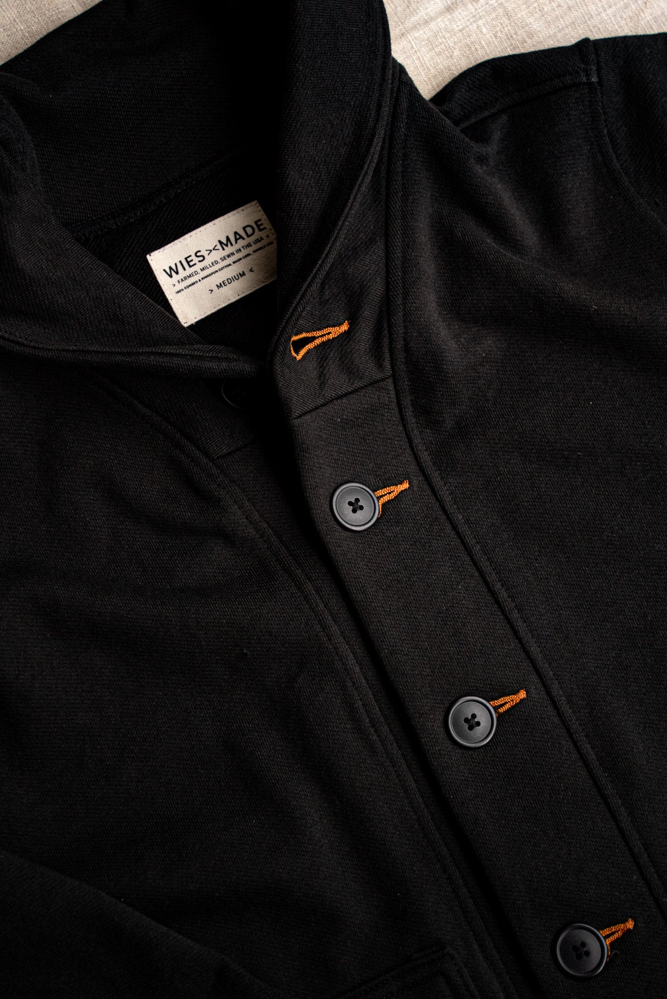 Close-up of black Bodega shawl cardigan with contrast orange tobacco-thread keyholes and matte buttons.