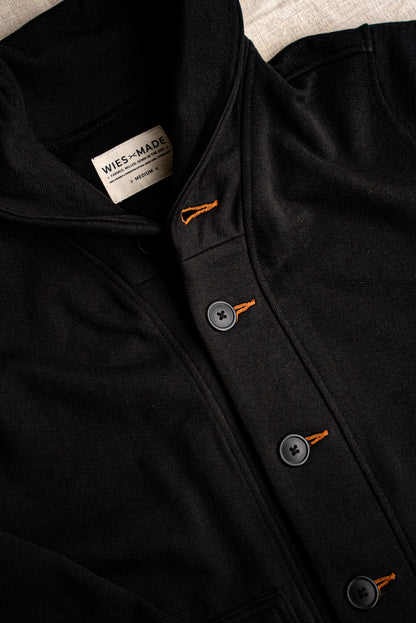 Close-up of black Bodega shawl cardigan with contrast orange tobacco-thread keyholes and matte buttons.