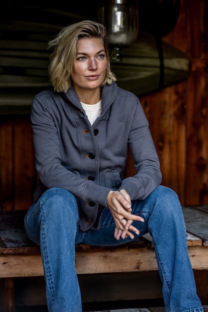 Woman seated on a wooden bench wearing the pebble gray Bodega shawl-collar French terry cardigan with tobacco keyhole.
