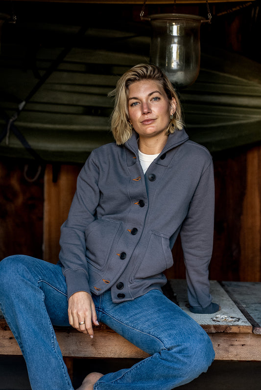 Woman in a pebble grey French terry shawl cardigan with tobacco contrast keyholes, paired with blue denim jeans.