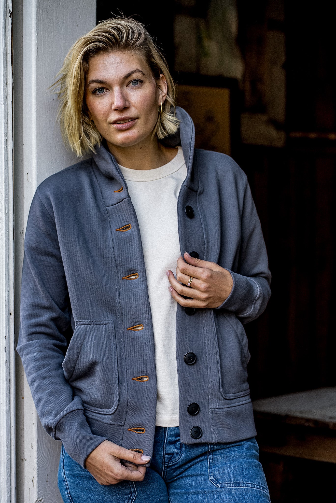 Woman wearing the pebble-gray Bodega shawl collar French terry cardigan with tobacco keyhole stitching over a cream tee and.