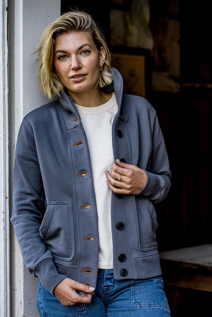 Woman wearing the pebble-gray Bodega shawl collar French terry cardigan with tobacco keyhole stitching over a cream tee and.