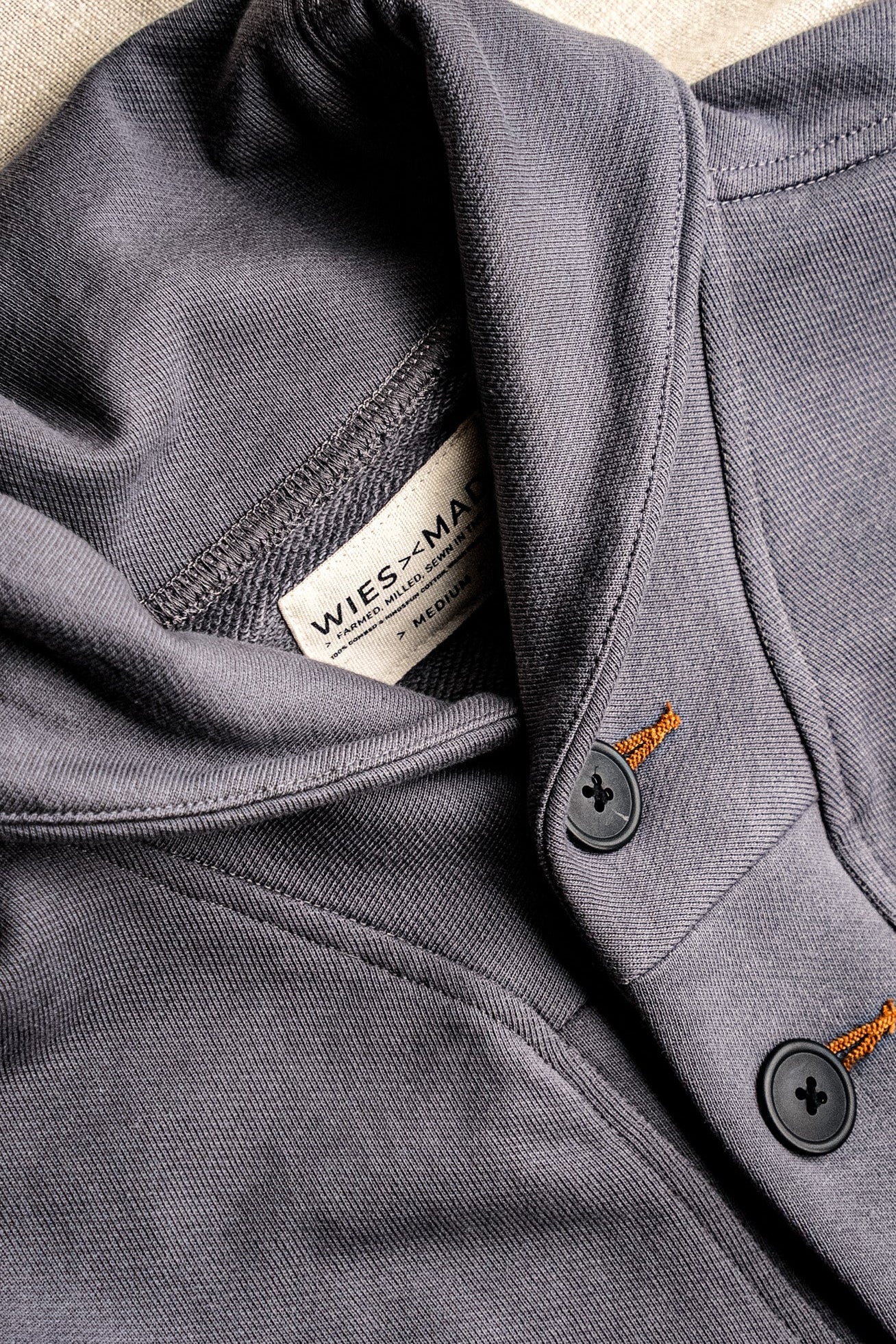 Close-up of pebble grey French terry cardigan showing shawl collar, WiesMade label, and tobacco-stitched keyhole buttons.