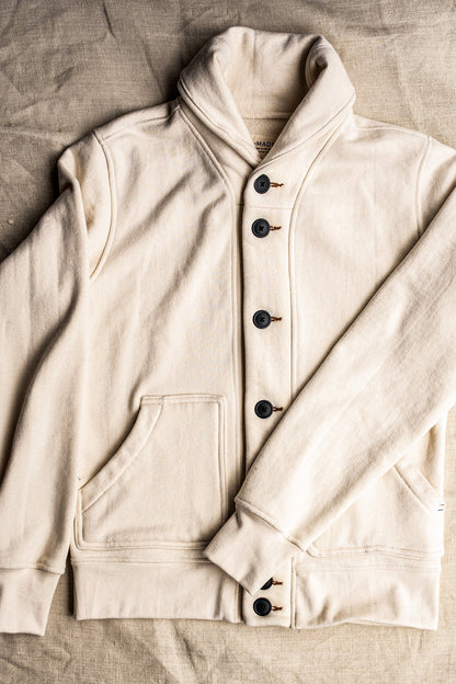 Natural French terry shawl-collar Bodega cardigan laid flat, showing dark buttons and front pocket.