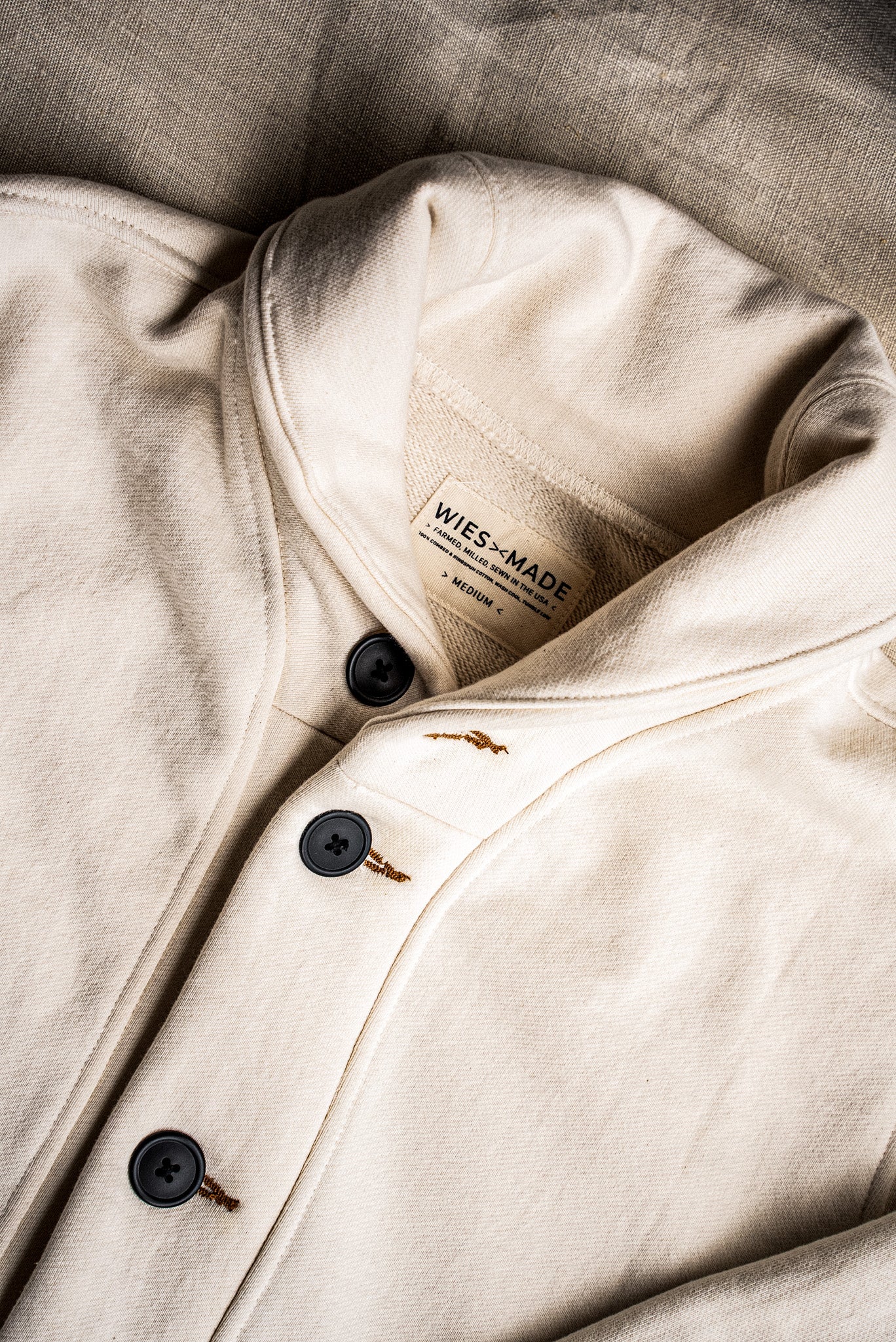 Close-up of natural cotton French terry cardigan with black buttons and tobacco keyhole stitching.