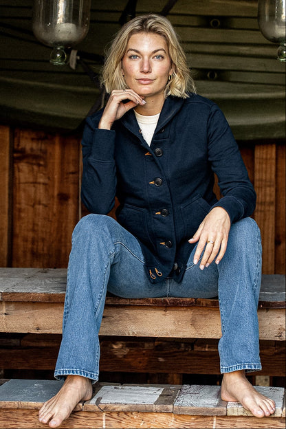 Woman wearing a buttoned navy French terry cardigan with tan keyholes, seated on wood steps.