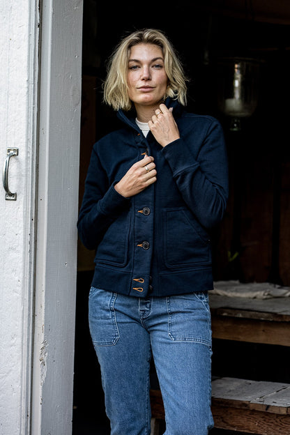 Woman wears the navy French terry Bodega cardigan with contrast tobacco keyholes over blue jeans.