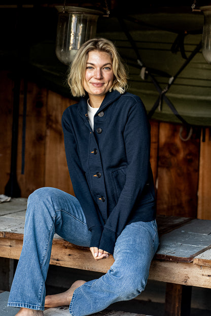 Person in navy French terry Bodega cardigan and jeans seated on a rustic wood bench.