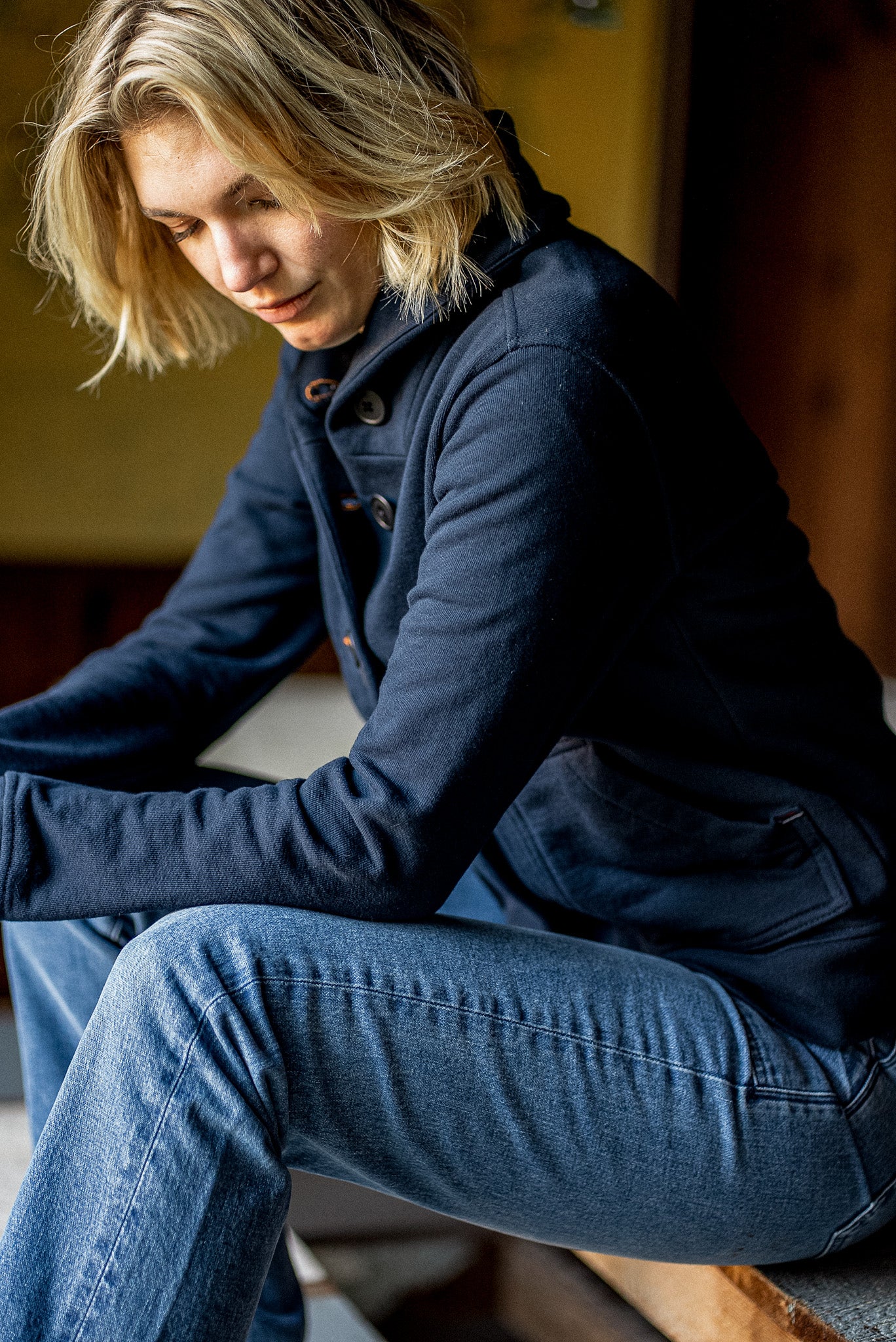 Navy French terry cardigan with contrast keyhole buttons, worn buttoned over jeans while seated.
