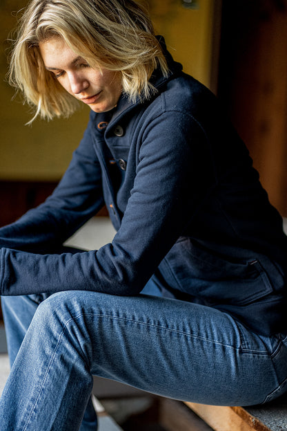 Navy French terry cardigan with contrast keyhole buttons, worn buttoned over jeans while seated.