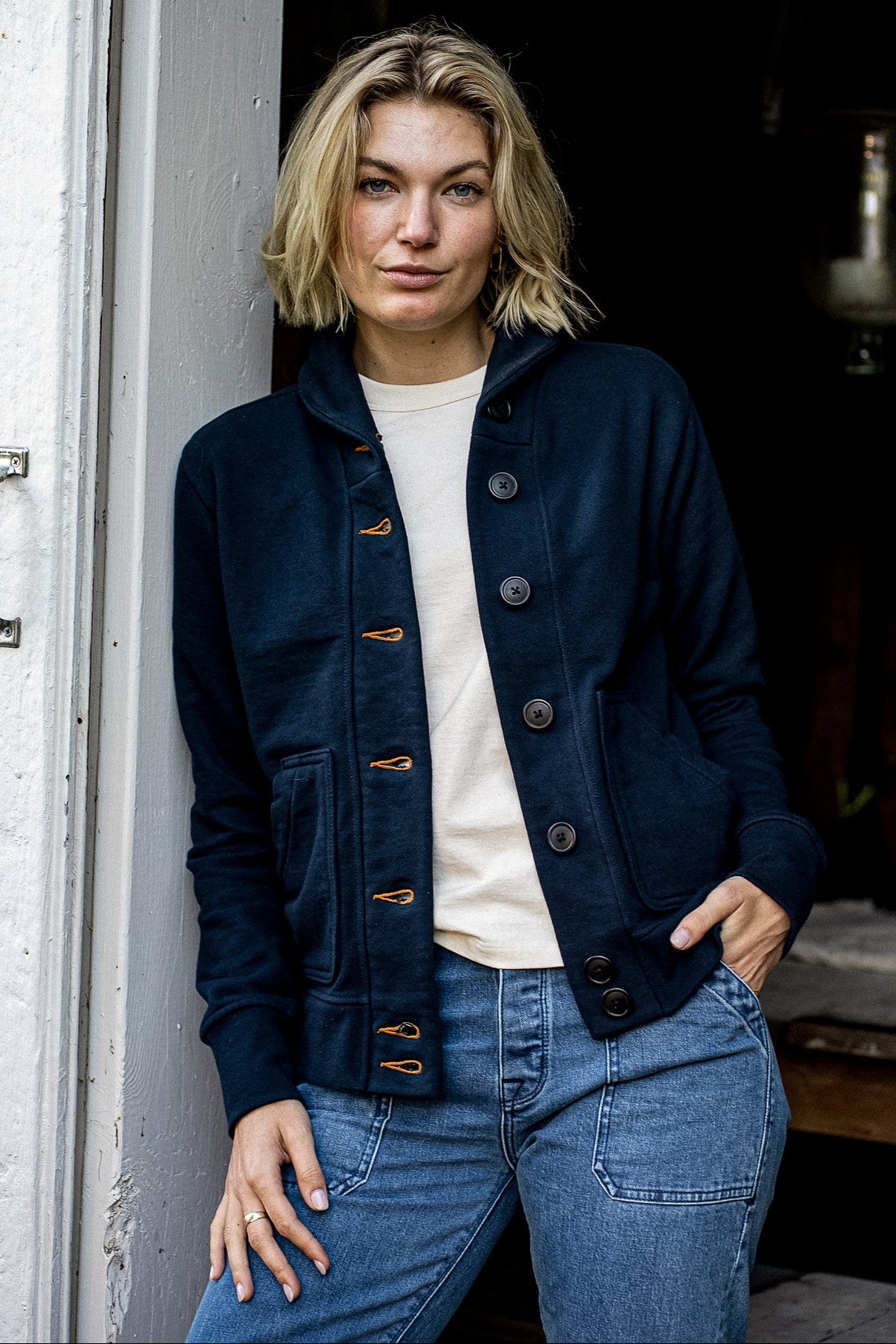 Navy French terry Bodega cardigan worn buttoned up with contrast tobacco keyhole stitching.
