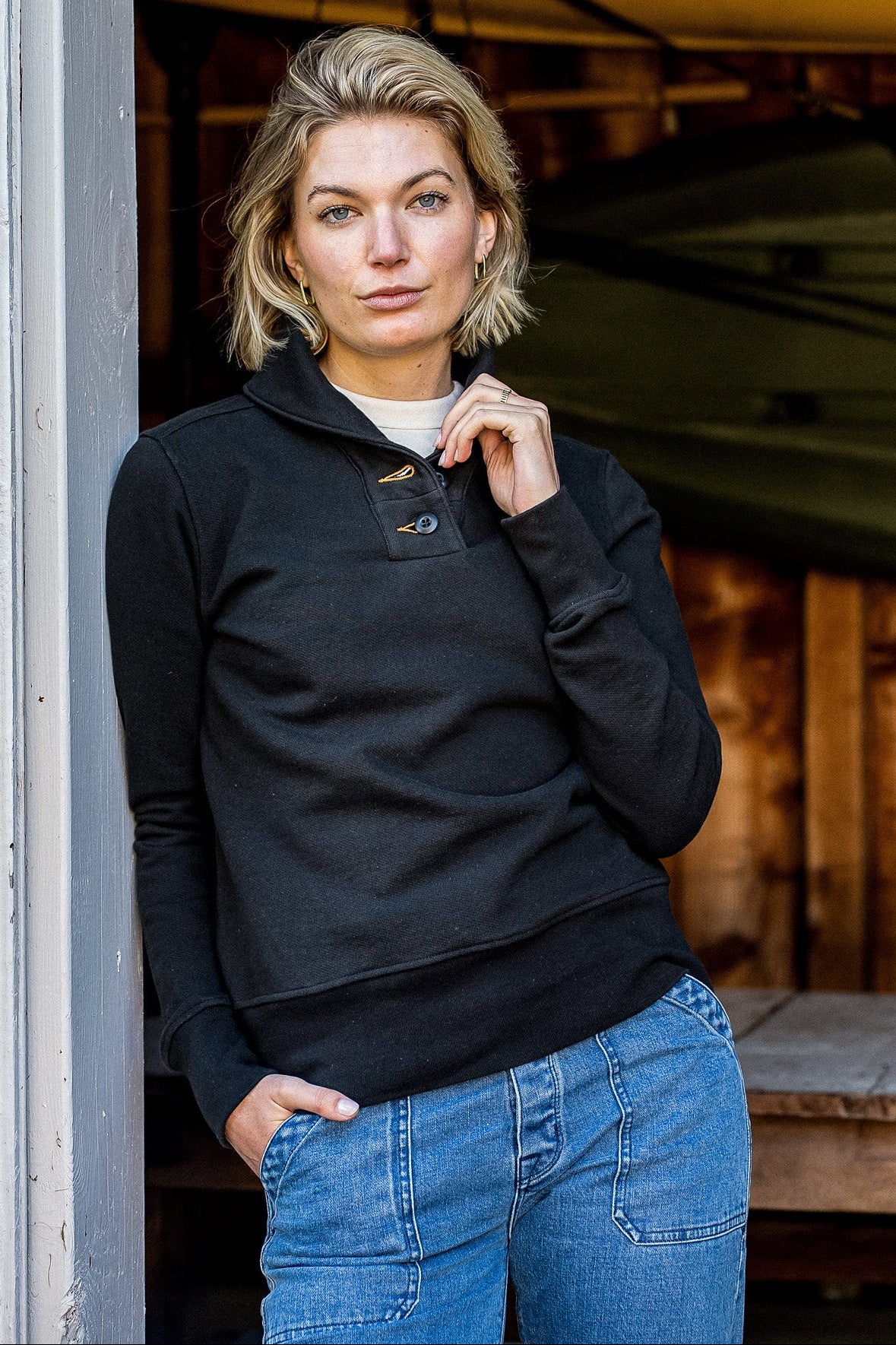 Woman wearing a black French terry shawl pullover with button placket, paired with blue jeans.