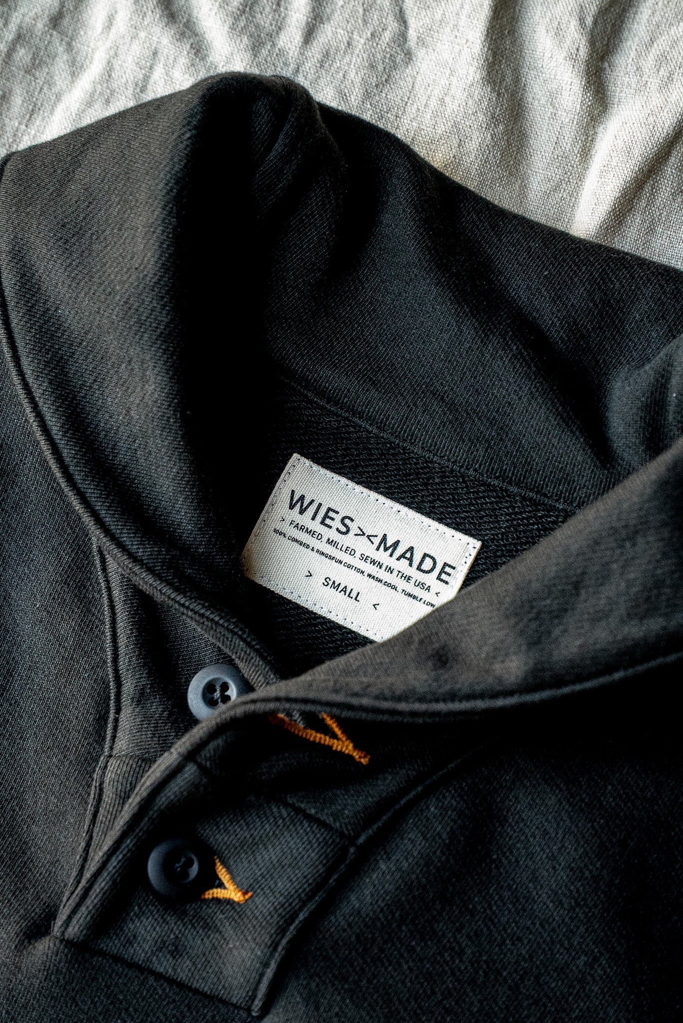 Close-up of the Basalt shawl collar pullover showing button placket, contrast gold stitching, and WiesMade USA-made label.