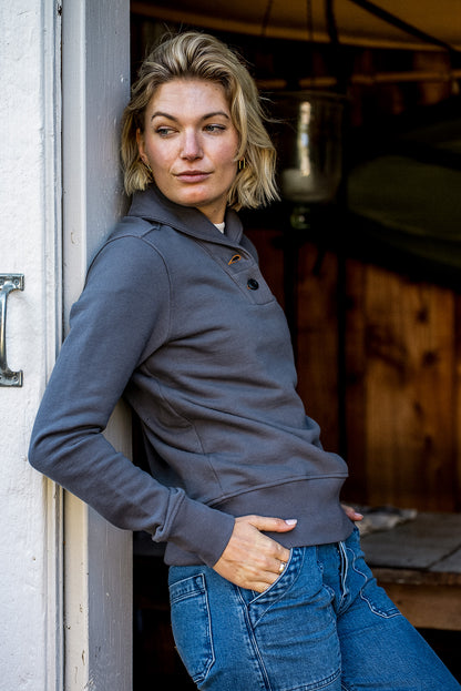 Woman leaning in a doorway wearing the gray Pebble Bodega shawl-collar French terry pullover.