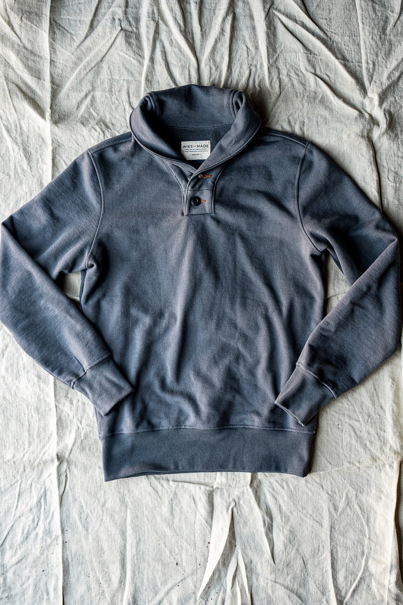 Pebble gray shawl collar French terry pullover laid flat on natural linen fabric.