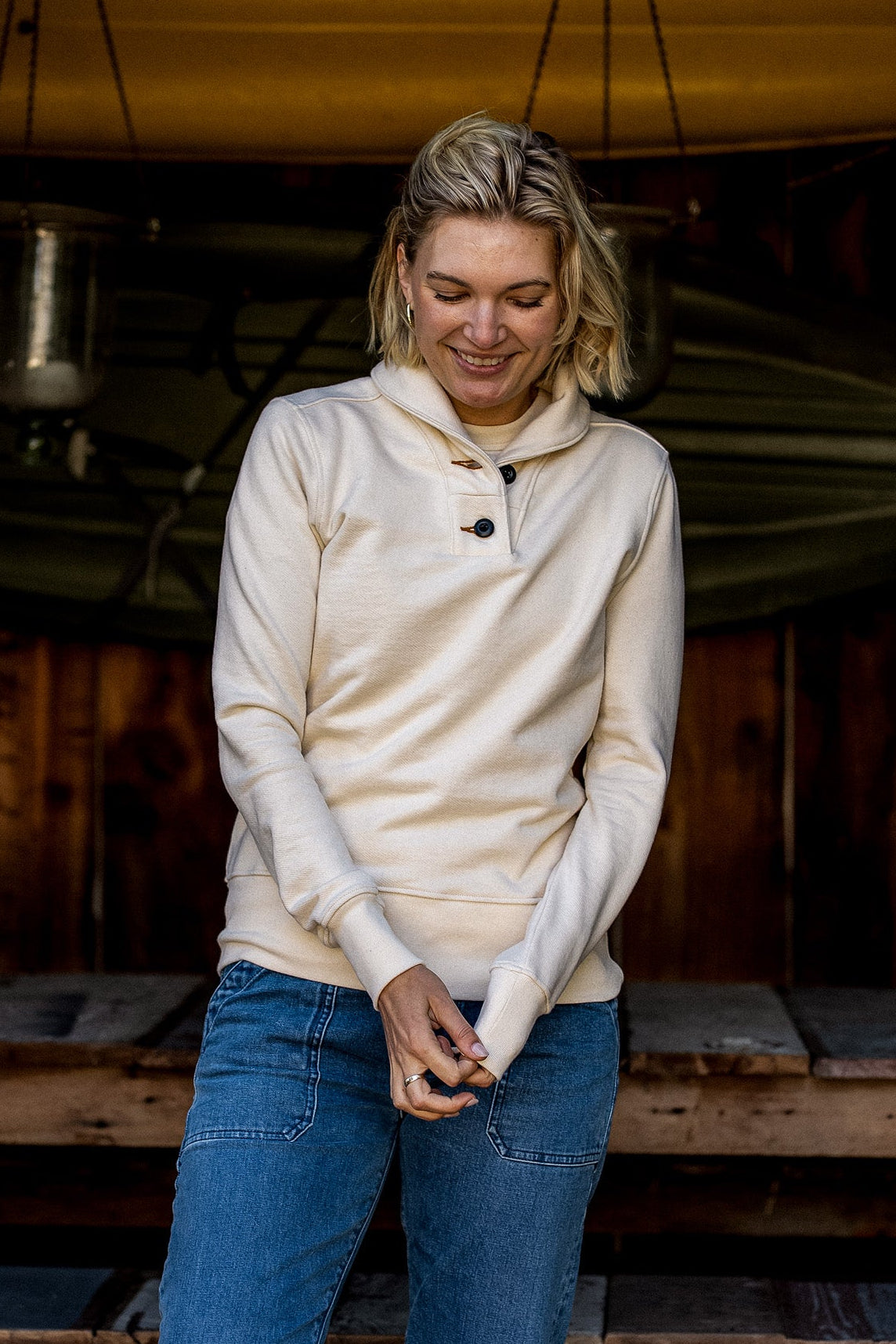 Woman wearing a natural cream French terry shawl collar pullover with button placket, paired with blue jeans.