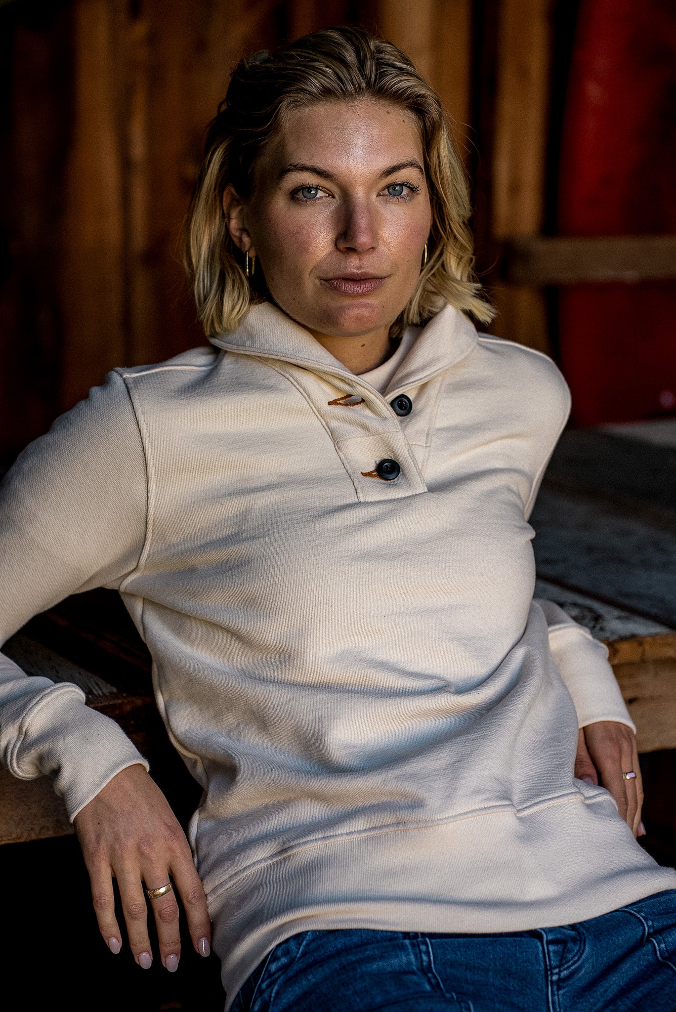 Model in a natural cotton French terry shawl-collar pullover with button placket, seated in a rustic barn.