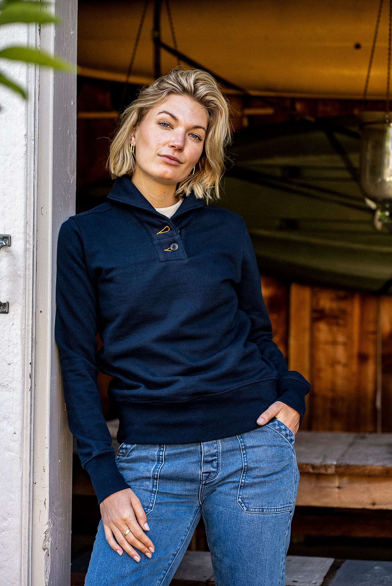 Person wearing navy Bodega shawl collar French terry pullover with jeans, leaning in a doorway.