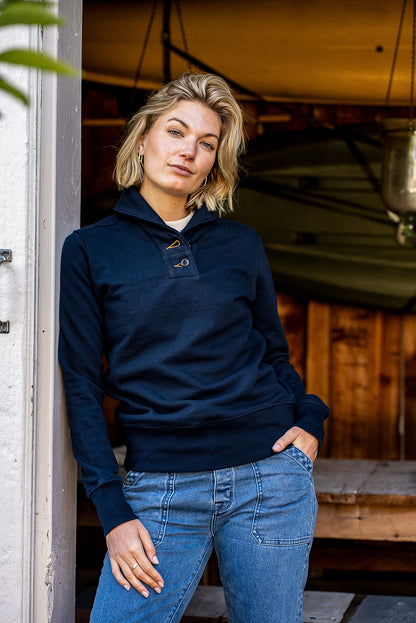 Person wearing navy Bodega shawl collar French terry pullover with jeans, leaning in a doorway.
