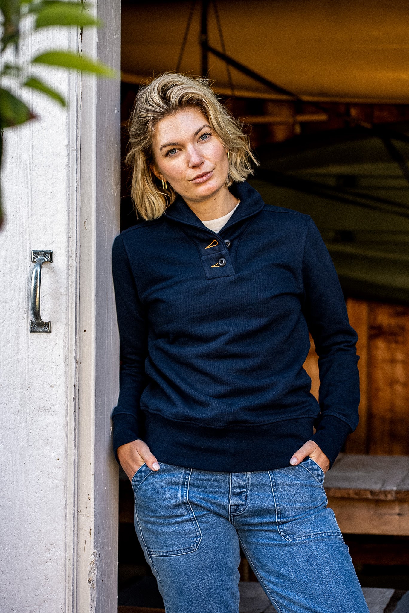 Person leaning in a doorway wearing the navy Bodega shawl pullover with jeans.