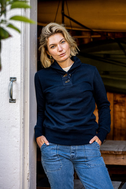 Person leaning in a doorway wearing the navy Bodega shawl pullover with jeans.