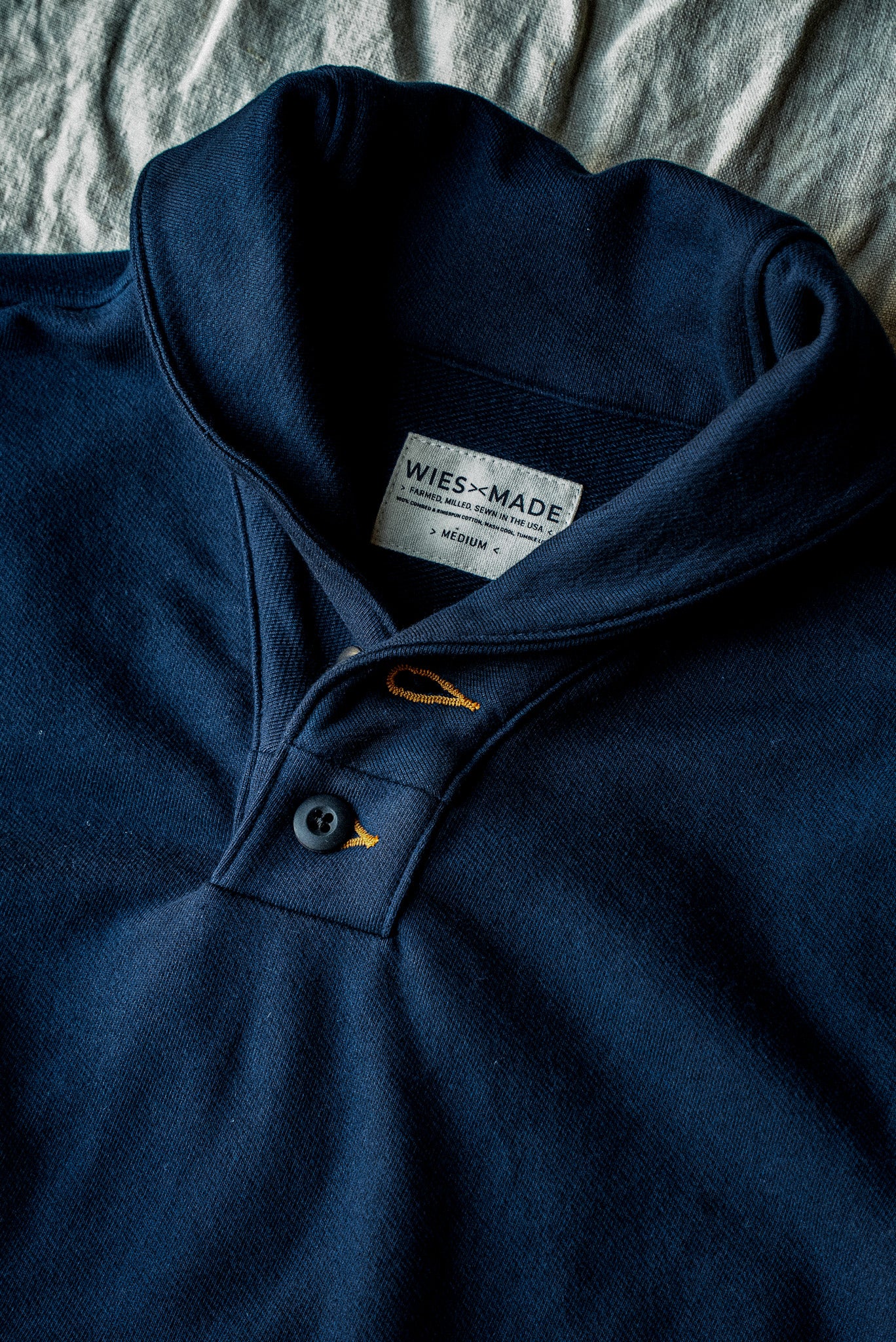 Navy French terry shawl collar pullover laid flat, showing button placket and WiesMade label.