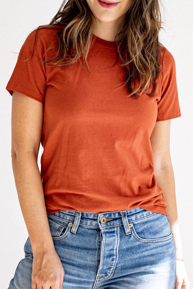 Woman wearing a brick-red heavyweight cotton crewneck tee tucked into light wash denim jeans.