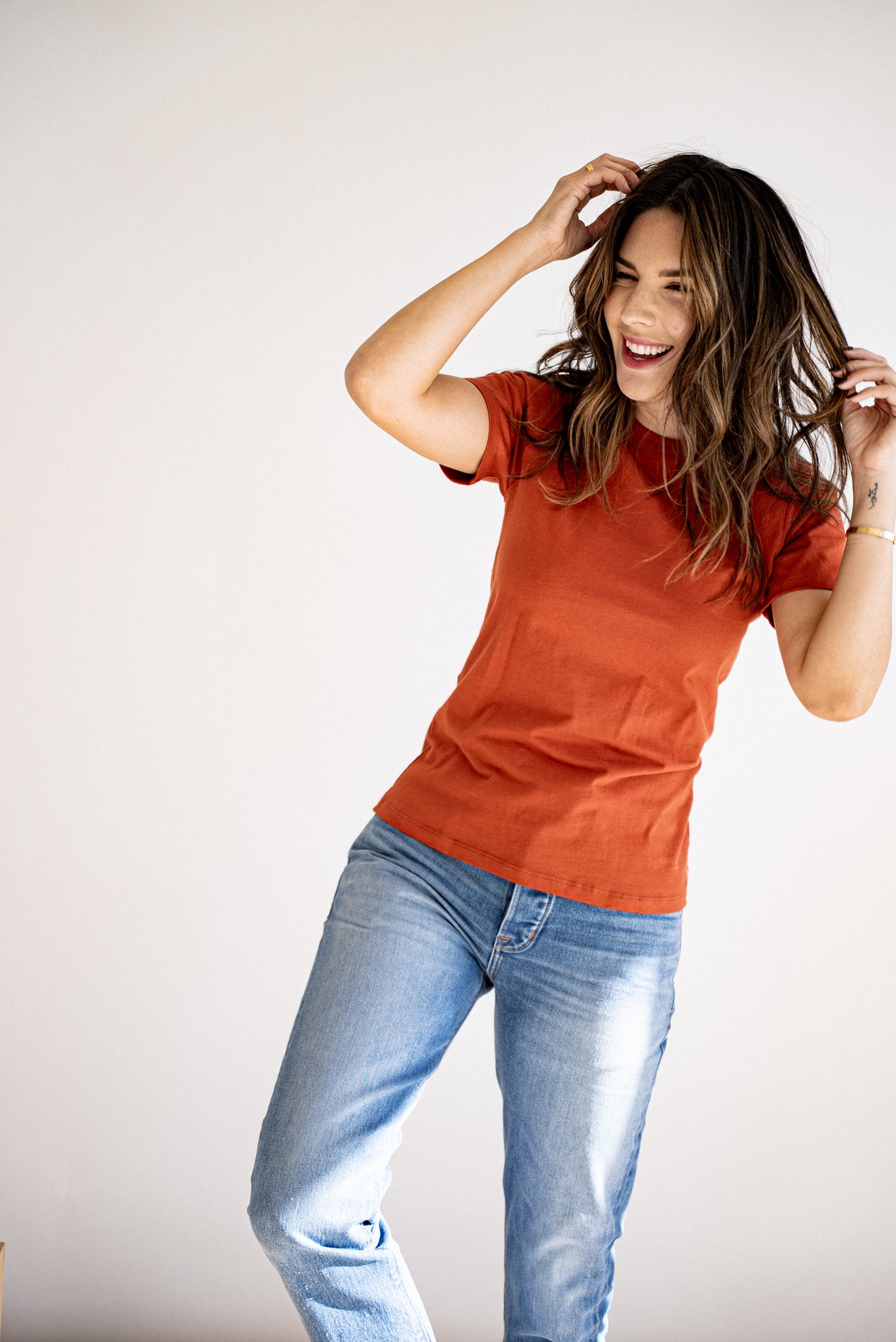 Woman laughing in a brick-colored heavyweight cotton crewneck tee paired with light-wash denim jeans.
