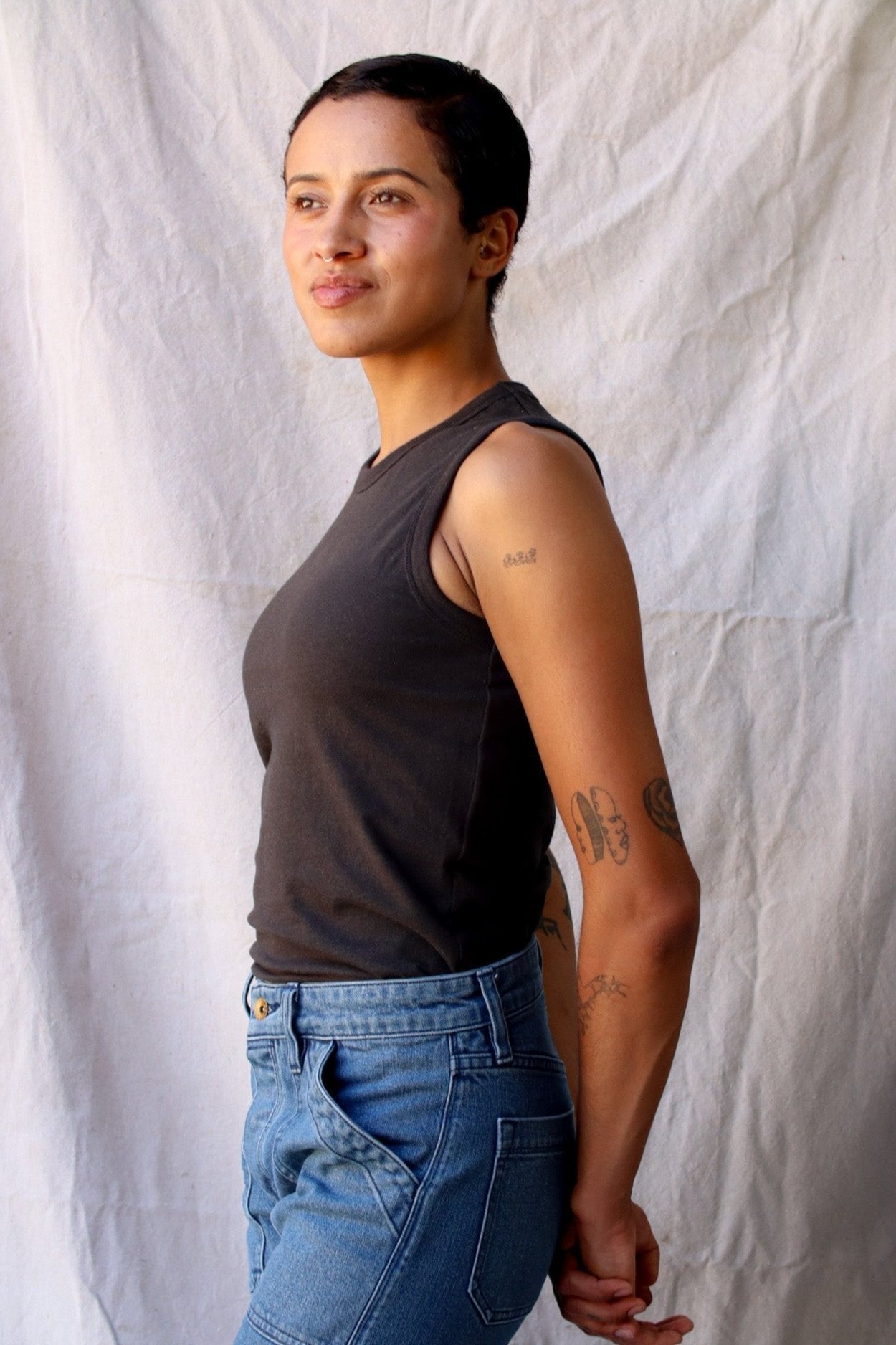 Side view of the Bolinas basalt cotton tank tucked into blue jeans against a linen backdrop.