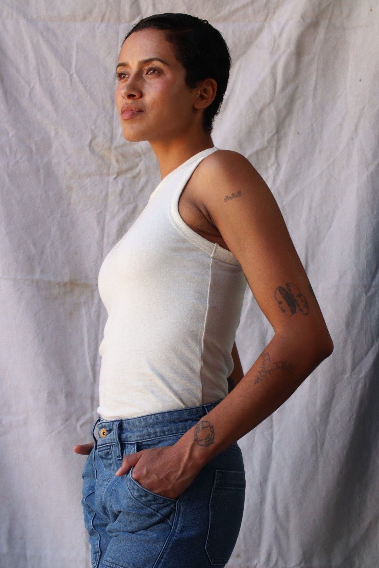 Side view of the natural cotton Bolinas tank tucked into blue denim jeans against a canvas backdrop.