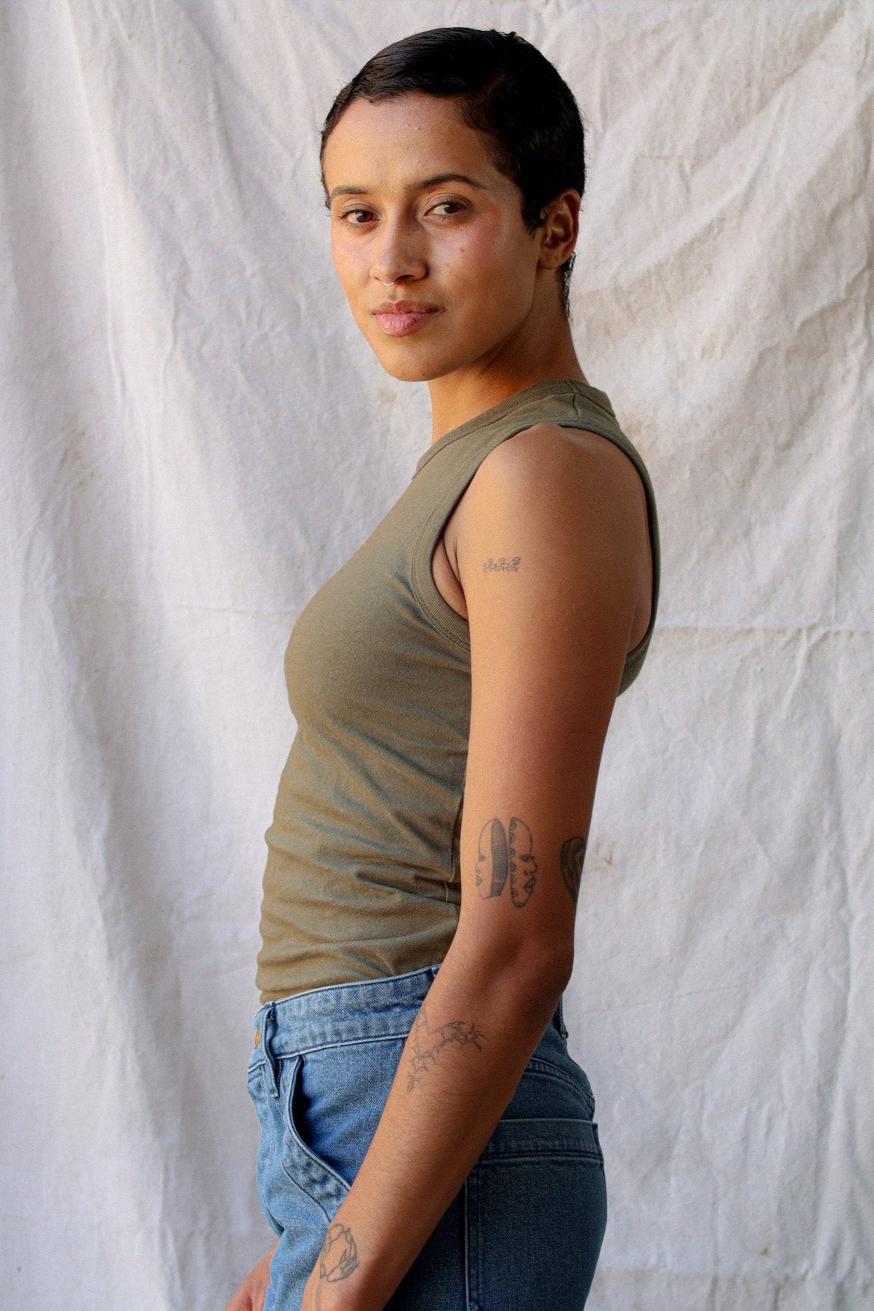Side view of the olive Bolinas cotton tank tucked into blue jeans against a white canvas backdrop.