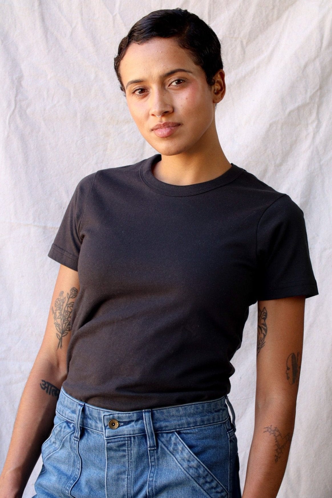 Model wearing the Bolinas heavyweight tee in basalt black with blue jeans against a linen backdrop.